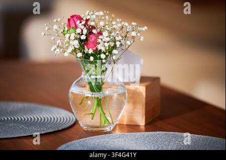 Strauß rosa Rosen in einer Glasvase mit Wasser auf dem Tisch, zarte Blüten mit Schleierkraut, gemütliche Inneneinrichtung, romantische Atmosphäre und Wohnstil Stockfoto