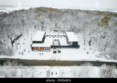 Luxuriöse moderne Häuser in der Winterlandschaft. Erhöhte Drohnenperspektive von geometrischen Gebäuden mit zentralem Innenhof und Pool, Autos am Straßenrand geparkt, Waldhintergrund, exklusives Wohnkonzept Stockfoto