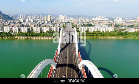 LIUZHOU, CHINA - 15. OKT. 2023: Luftaufnahme, die direkt entlang einer weißen Bogenbrücke verläuft, die den türkisfarbenen Liu-Fluss in Liuzhou, Guangxi, China, überquert. Stockfoto