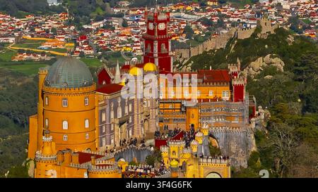 SINTRA, PORTUGAL - 12. APR 2025: Luftaufnahme aus hohem Winkel der gelben und roten Türme des Palastes von Pena mit maurischen Burgmauern in Sintra, Portugal. Stockfoto