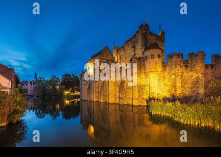 Gravensteen, eine mittelalterliche Burg in der Stadt Gent in Belgien, Europa. Historische Steinfestung bei der Dämmerung beleuchtet, gespiegelt im ruhigen Wassergraben Stockfoto