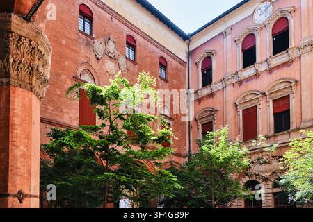 Bologna, Italien – Mai 2026: Innenhof des Palazzo d'Accursio mit historischer Terracotta-Fassade, Uhr und geschnitzter Steinsäule Stockfoto