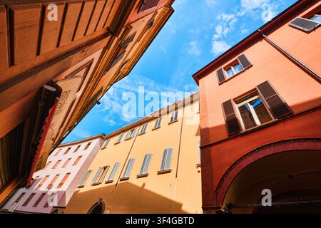 Bologna, Italien - Mai 2026: Niedriger Blick aus der Froschperspektive auf farbenfrohe terrakottafarbene historische Gebäude, die den blauen Himmel einrahmen Stockfoto