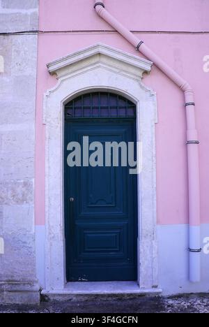 Eine dunkelgrüne Holztür mit einem dekorativen steinernen Rahmen steht in einer pastellrosa Gebäudefassade in Lissabon, Portugal Stockfoto
