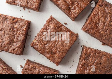 Schokoladen-Zucchini-Brownie-Quadrate auf weißem strukturiertem Hintergrund, Oberansicht. Flachlage, horizontal Stockfoto