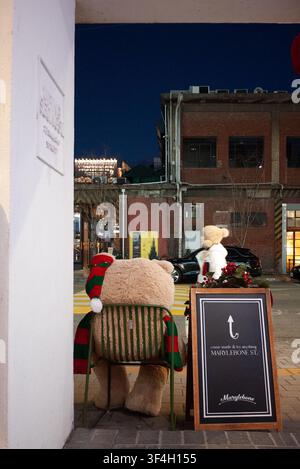 Ein großer Teddybär mit einem Weihnachtsschal sitzt auf einem Stuhl auf einer Straße in Seongsu-dong, Seoul. Stockfoto