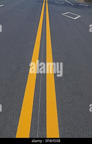 Diese Aufnahme zeigt eine detaillierte Nahaufnahme von doppelten durchgehenden gelben Linien auf einer dunklen Asphaltstraßenoberfläche. Das scharfe, lebendige Gelb Stockfoto
