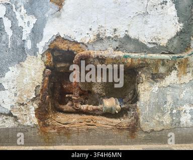 stark verrostete und verkrustete Rohre, die durch eine bröckelnde, verwitterte Wand ragen. Alternde Infrastruktur in der Mirador-Villa, Hongkong Stockfoto