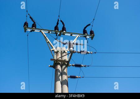 Beton-Elektrizitätsverteilungsmast mit Isolatoren und Freileitungen, von unten gegen einen klaren blauen Himmel betrachtet Stockfoto