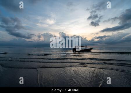Dramatischer Sonnenaufgang über einem friedlichen Ozean, mit einem traditionellen Langkielboot, das sich als Silhouette gegen einen Himmel voller schöner Wolken abhebt. Warmes Licht reflektiert Stockfoto