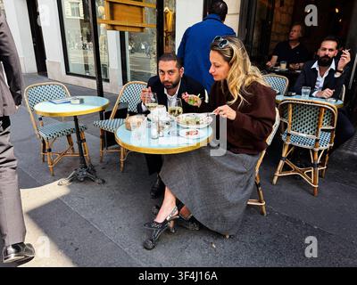 Paris, Frankreich - 14. Mai 2026: Ein Paar und Freunde genießen Mittagessen und Wein in einem geschäftigen Pariser Straßencafé an einem sonnigen Gehweg. Stockfoto