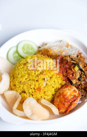 Indonesischer Kurkuma-Reis oder nasi kuning ist aromatischer Reis, der mit Kurkuma und aromatischen Gewürzen zubereitet wird und mit traditionellen Beilagen serviert wird Stockfoto