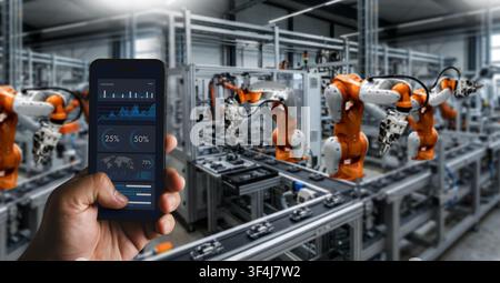 Ingenieure testen das Steuerpult auf einem Smartphone, um Roboterarme in einer automatisierten Fabrik zu überwachen, was die industrielle Automatisierung und Produktionsunterstützung fördert Stockfoto