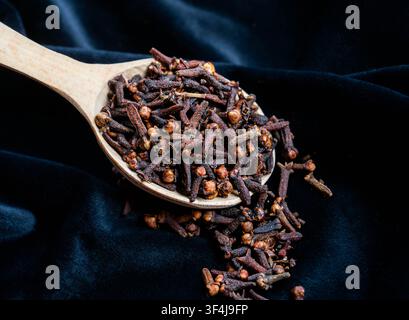 Ganze getrocknete Nelken in einem Holzlöffel auf schwarzem Samtgrund. Aromatisches Gewürz zum Kochen, Backen und für heiße Getränke. Stockfoto