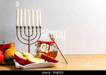 Rosh Haschanah-Symbole einschließlich einer Menora, Honig, Äpfel und Granatäpfel auf einem Holztisch Stockfoto