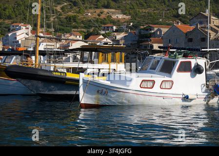 Kleines hölzernes Fischerboot und aufblasbare Festrumpfboote, die in einem Hafen festgemacht sind, mit traditionellen Häusern mit roten Ziegeldächern und kiefernbewachsenen Hügeln im Hintergrund Stockfoto