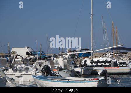 Kleines Holzruderboot, das in einer belebten mediterranen Marina vertäut ist, umgeben von verschiedenen Motorbooten, Schnellbooten und Segeljachten an einem klaren Sonnentag. Stockfoto