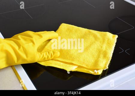 Person in gelbem Handschuh, der Induktionsherd mit gelbem Tuch reinigt Stockfoto