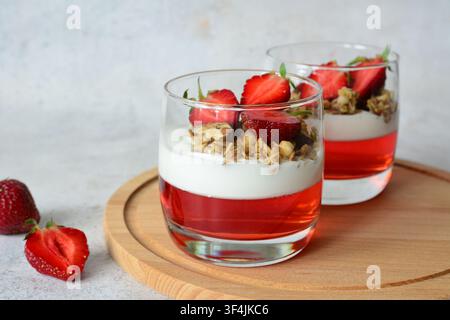 Erdbeer-Dessert mit Gelee, Granola und Joghurt in Gläsern auf Holzbrett Frontansicht Stockfoto