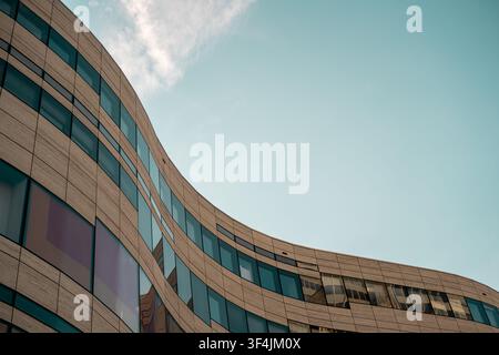 Gekrümmte moderne Gebäudefassade mit Glasfenstern und großem blauem Himmel als Kopierraum Stockfoto