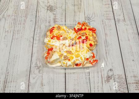 Deviled Eggs mit Thunfisch, Mayonnaise und gewürfelten roten Paprika, verpackt in einem klaren Plastikbehälter auf gekalktem Holz. Stockfoto