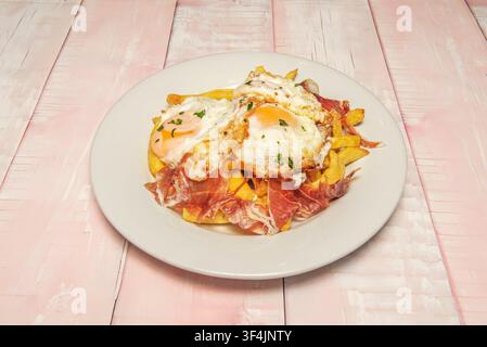 Spiegeleier mit flüssigem Eigelb über knusprigen Pommes, geschichtet mit Scheiben spanischen Schinkens, garniert mit Petersilie. Stockfoto
