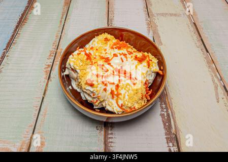 Gefüllte Eier, die in Mayonnaise ertränkt sind, mit geriebenem Eigelb und geraspelter Karotte belegt, serviert in einer braunen Keramikschale. Stockfoto