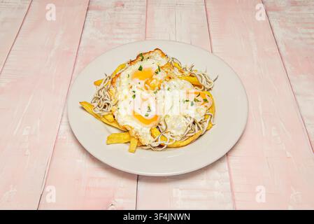 Zerbrochene gebratene Eier und zarte Baby-Aale, die über goldenen Pommes frites aufgeschichtet sind, mit frischen gehackten Kräutern bestreut. Stockfoto