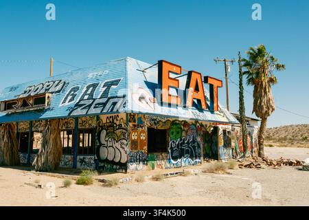 Ein verlassenes, mit Graffiti bedecktes Raststättenrestaurant mit einem auffälligen EAT-Schild steht in der Wüste, Halloran Springs, Kalifornien Stockfoto