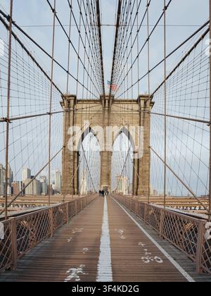Blick auf die Brooklyn Bridge mit ihren ikonischen Steinbögen, Stahlseilen und hölzernem Fußgängerweg, im Hintergrund die Skyline von Manhattan Stockfoto