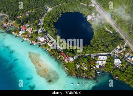 Luftaufnahme des Cenote Cocalitos mit seinen tiefblauen Gewässern, die sich von der türkisfarbenen Lagune abheben, umgeben von üppiger Vegetation und Uferpromenade Stockfoto