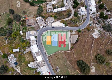 Luftbild eines farbenfrohen Sportplatzes im Dorf Apeiranthos auf der Insel Naxos, Griechenland, umgeben von kurvenreichen Straßen, weißen Häusern und terrassierten Feldern Stockfoto
