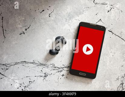 Mobiltelefon, das ein Videoplayer-Logo mit kabellosen Kopfhörern anzeigt, repräsentiert die digitale Mediennutzung und Online-Streaming Stockfoto