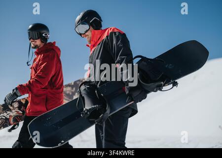 Zwei Snowboarder tragen ihre Bretter auf einem verschneiten Berghang unter einem klaren blauen Himmel Stockfoto