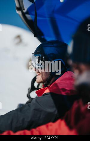Mann mit Helm und Schutzbrille auf dem Skilift, der auf die schneebedeckte Berglandschaft schaut Stockfoto
