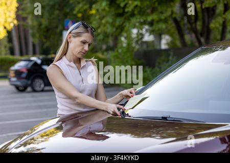 Frau, die einen Parkverwehticket auf der Windschutzscheibe des Autos in einem öffentlichen Parkplatz erhält Stockfoto