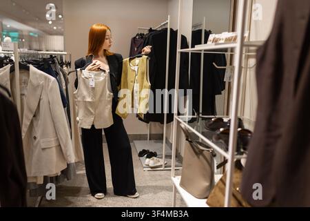 Frau vergleicht zwei Westen beim Einkaufen in einem Modegeschäft Stockfoto