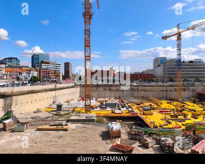 Eine große städtische Baustelle mit einem Fundamentgraben, hohen gelben Kränen und modernen Stadtgebäuden unter einem blauen Himmel, mit Fokus auf industrielles Wachstum Stockfoto