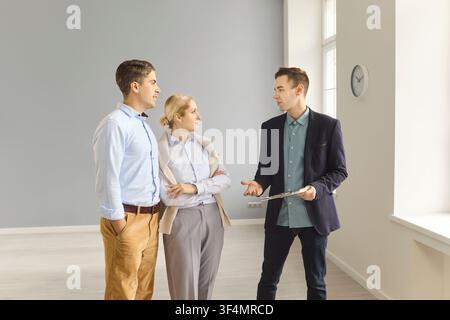 Immobilienmakler berät ein Paar während einer Wohnungsbesichtigung in einem hellen, leeren Raum Stockfoto