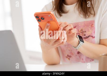 Kiew, Ukraine. 29. Juli 2026. Nahaufnahme der Hände einer Frau, die ein orangefarbenes iPhone 17 Pro Max hält und damit interagiert. Fokus auf die Rückkamera. Stockfoto
