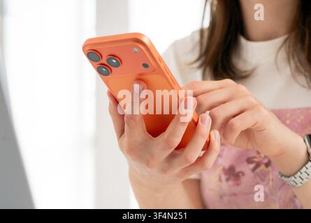 Kiew, Ukraine. 29. Juli 2026. Nahaufnahme der Hände einer Frau, die ein orangefarbenes iPhone 17 Pro Max hält und damit interagiert. Fokus auf die Rückkamera. Stockfoto