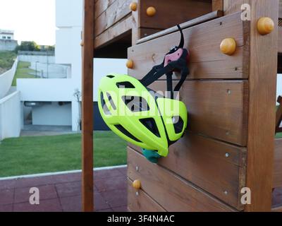 Heller Fahrradhelm an einer hölzernen Kletterwand in einem öffentlichen Spielplatz. Sicherheitsausrüstung für Kinder, die Outdoor-Aktivitäten und Freizeit genießen. Stockfoto