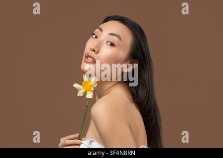 Junge asiatische Frau hält eine Blume, lächelt, elegante Pose, Schönheitskonzept Stockfoto