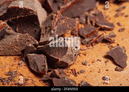 Nahaufnahme von zerbrochenen Stücken dunkler Schokolade mit rauer Textur, die über eine Holzoberfläche verstreut sind, was auf Backen oder Süßwarenproduktion hindeutet Stockfoto