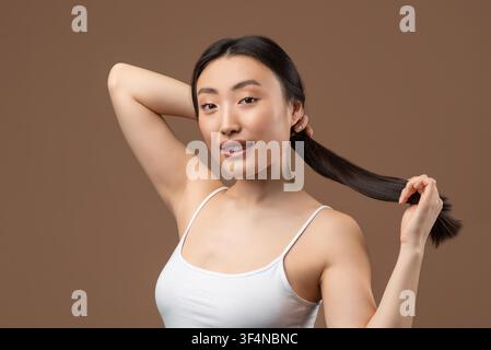 Junge asiatische Frau lächelt und spielt mit langen Haaren, Studiohintergrund, Schönheitskonzept Stockfoto