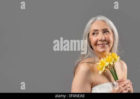 Lächelnde ältere Frau mit gelben Blumen, Porträt, glücklich und fröhlich Stockfoto