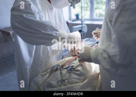 Medizinisches Team von Chirurgen führt einen komplexen Eingriff an einem Patienten in einem sterilen Operationssaal durch, wobei Instrumente sichtbar sind. professioneller Neurochirurg Stockfoto