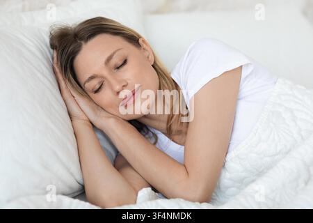 Junge Frau schläft bequem im Bett mit weichen Kissen und warmer Decke Stockfoto