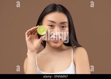 Junge asiatische Frau lächelt und hält eine Limettenscheibe, Konzept für einen gesunden Lebensstil Stockfoto