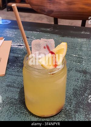 Ein erfrischendes gelbes Getränk, das in einem klaren Glas-Mason-Glas serviert wird, steht auf einer verwitterten tealfarbenen Holzoberfläche. Das Getränk scheint zu sein Stockfoto